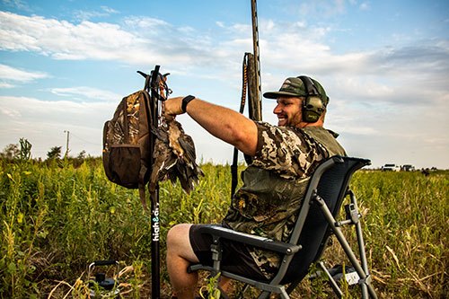 Dove hunter sitting in lawn chair in field.