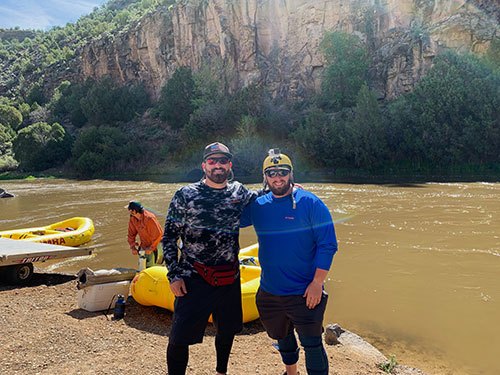 Snapshot of two guys with rafts and river in background.